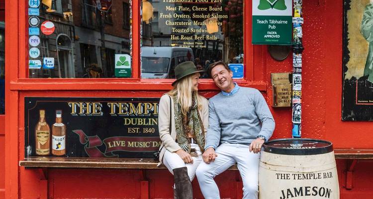 Una pareja sonriente se sienta afuera del famoso pub rojo Temple Bar de Dublín tomados de la mano.