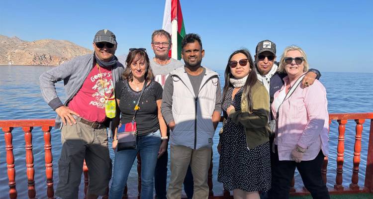 Grupo de personas en un barco con bandera y fondo montañoso.