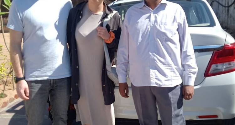 Ein lockeres Foto im Freien mit drei Personen und einem geparkten Auto im Hintergrund.