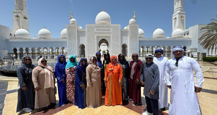 Groupe de personnes en tenue traditionnelle devant une grande mosquée blanche.