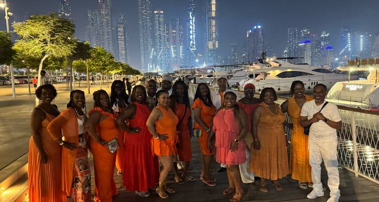 Groupe de personnes en tenue orange posant au bord de l'eau avec des bâtiments modernes éclairés.