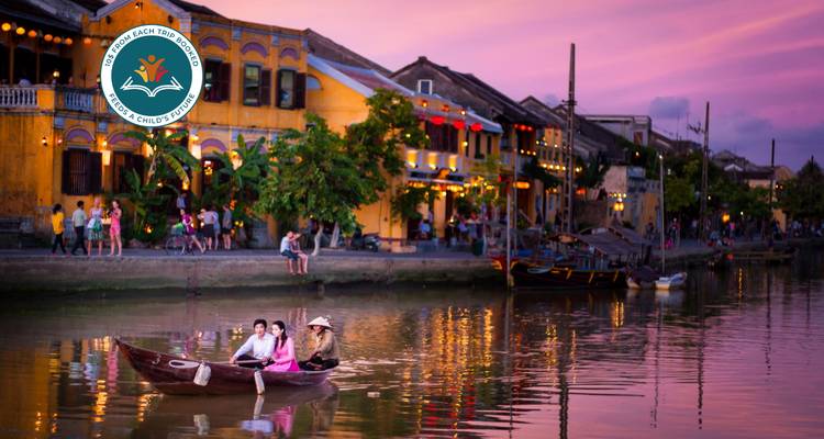 Personnes naviguant sur une rivière au coucher du soleil avec des bâtiments vietnamiens traditionnels.