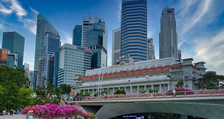 Horizon moderne de Singapour avec des tours de grande hauteur derrière l'hôtel colonial Fullerton et un pont bordé de bougainvilliers roses.