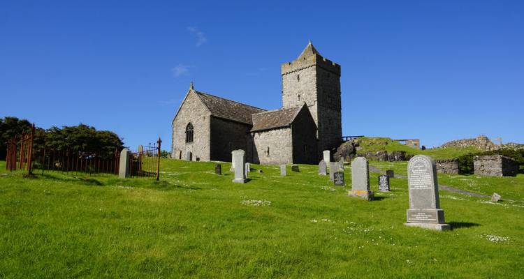 Église en pierre historique avec cimetière sous un ciel bleu dégagé.