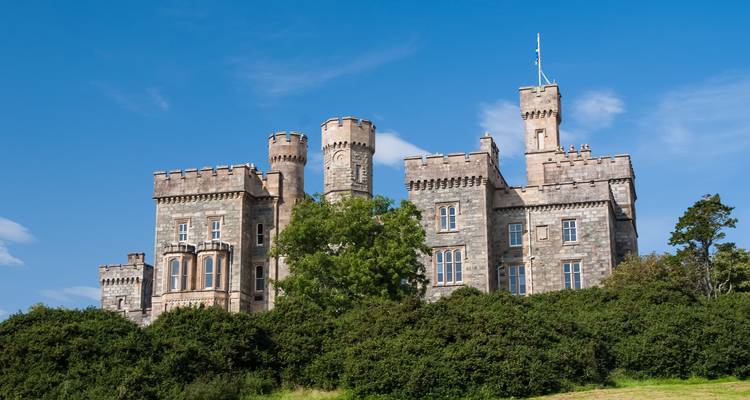 Château sur une colline entouré d'arbres sous un ciel bleu.