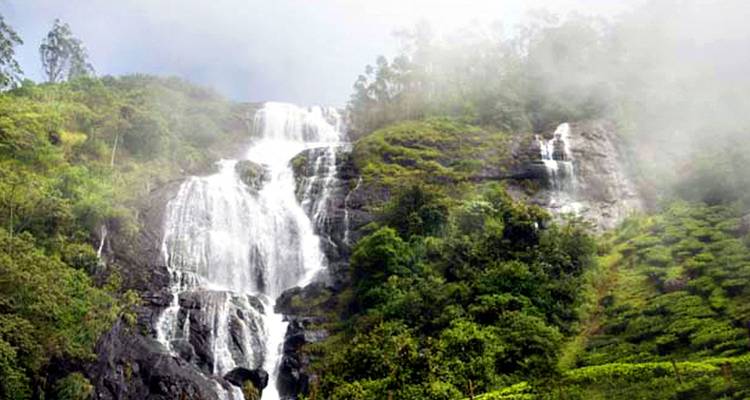 Waterfall cascading down green hills on a misty day.