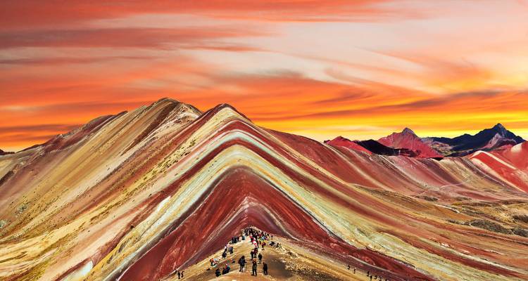 Rainbow Mountains with hikers under a vibrant sunset sky.