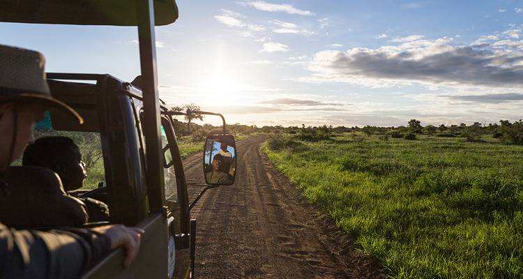 Véhicule de safari sur une route de terre au coucher du soleil.
