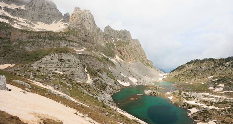 Bergsee umgeben von felsigen Gipfeln und Schneeflecken.