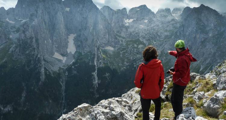 Zwei Wanderer in roten Jacken blicken auf dramatische Felsengebirge.