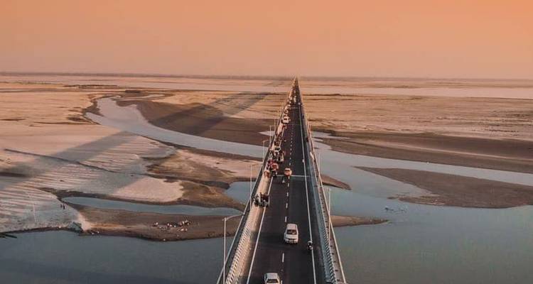 Long pont droit enjambant une vaste étendue d'eau au coucher du soleil.