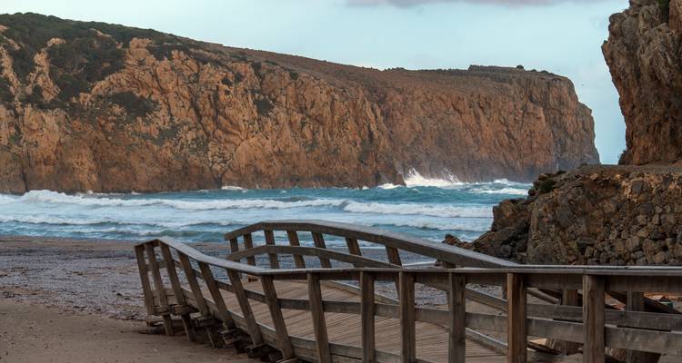 Passerelle en bois menant à un océan orageux et à des falaises.