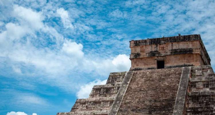 Stenen pyramidetrap die omhoog leidt naar een klein tempel tegen een helderblauwe lucht met verspreide wolken