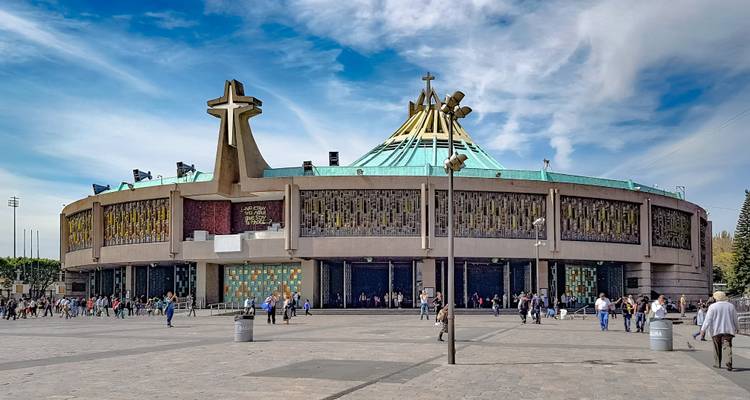 Ronde basiliek met kruis onder een helderblauwe hemel op een groot geplaveid plein vol bezoekers