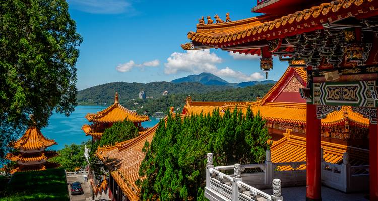 Scenic view of traditional Taiwanese architecture with mountains and a lake in the background.