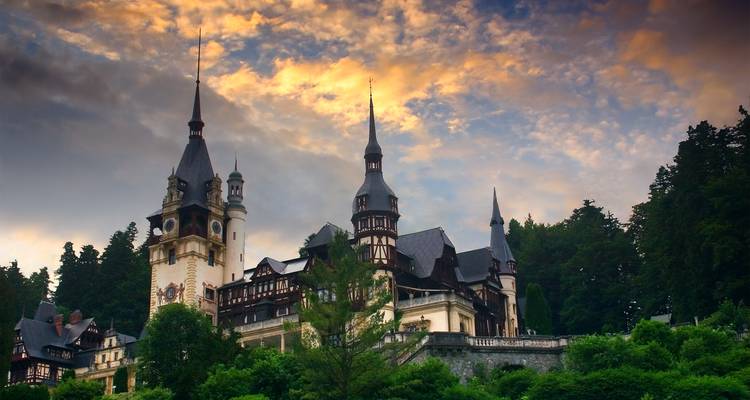 Le château de Peles se dressant contre un ciel du soir dramatique, entouré de collines boisées.