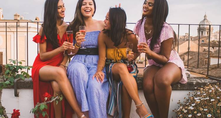Cuatro mujeres sentadas disfrutando bebidas en una terraza con vista a la ciudad.