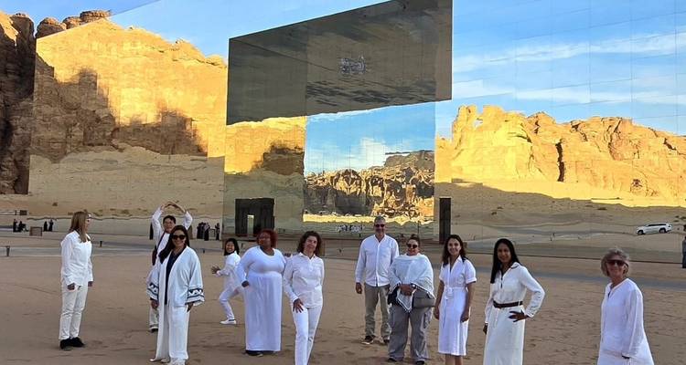Groupe de personnes en tenues blanches devant un bâtiment à miroirs situé dans un désert.