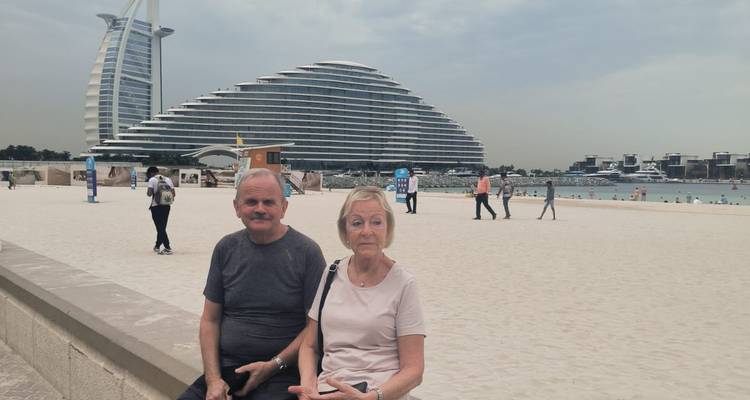 Couple sitting on a beach with a large modern hotel in the background.