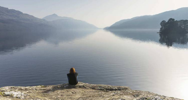 Personne assise sur un rocher surplombant un lac calme.
