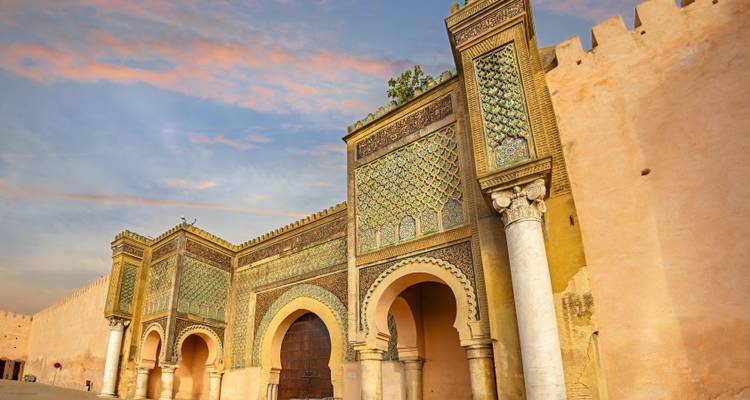 Majestic city gate with intricate mosaics against a sunset sky.