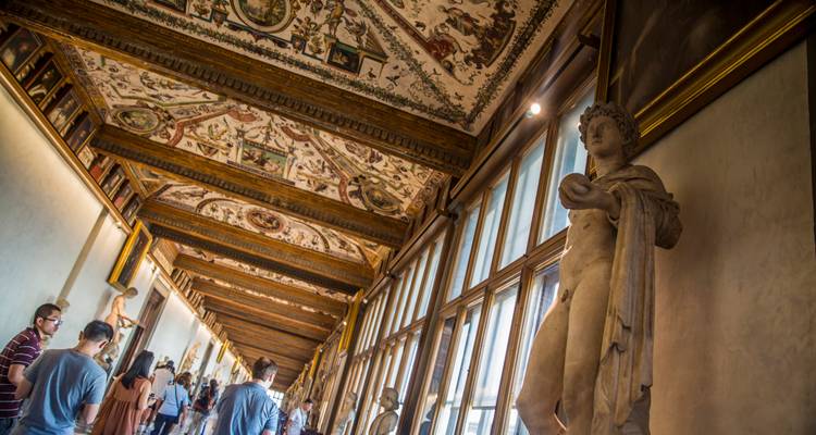Long corridor de galerie ornée avec plafond peint et statues classiques, des visiteurs circulant dans les lieux.