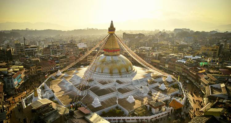 Aerial view of a stupa with prayer flags and the surrounding city.