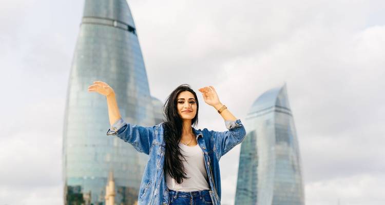 Frau posiert mit erhobenen Armen vor modernen Wolkenkratzern.