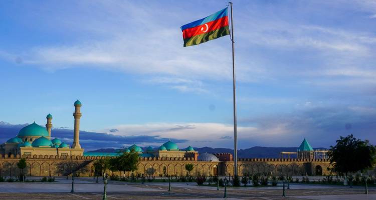 Aserbaidschanische Flagge weht über einer Moschee mit blauen Kuppeln.