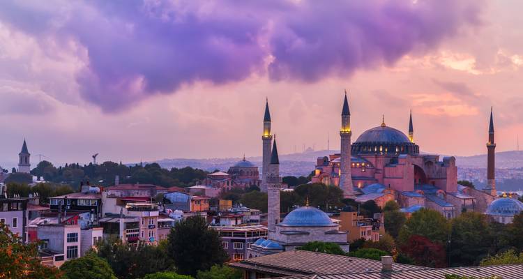 Schemerskyline van Istanbul met de iconische koepels and minaretten van de Hagia Sophia die boven de stad uitrijzen onder paars-roze wolken.