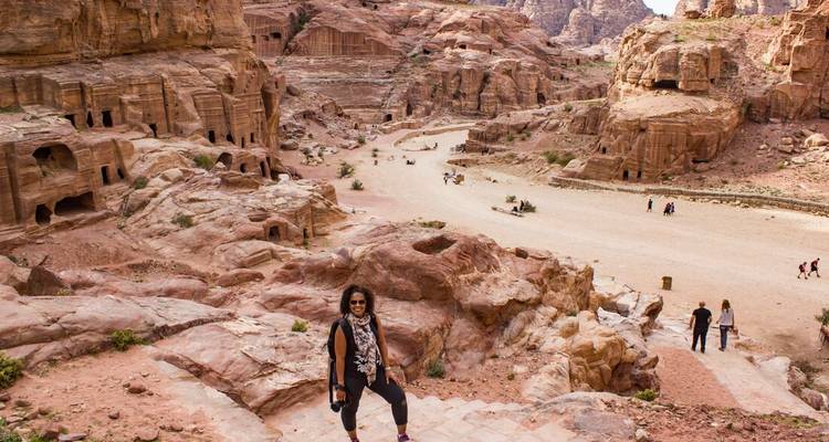 A woman sitting on ancient stairs with Petra in the background.