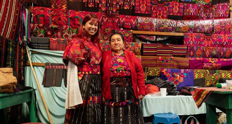 Deux femmes en vêtements traditionnels devant des textiles colorés.