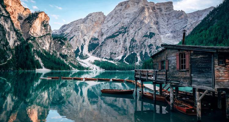 Scenic lake surrounded by mountains with a rustic wooden boathouse.