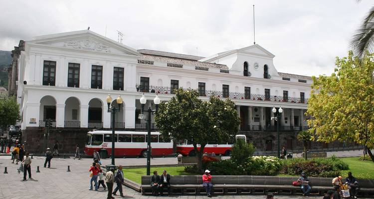 Colonial building with people and a red-white bus in Quito.