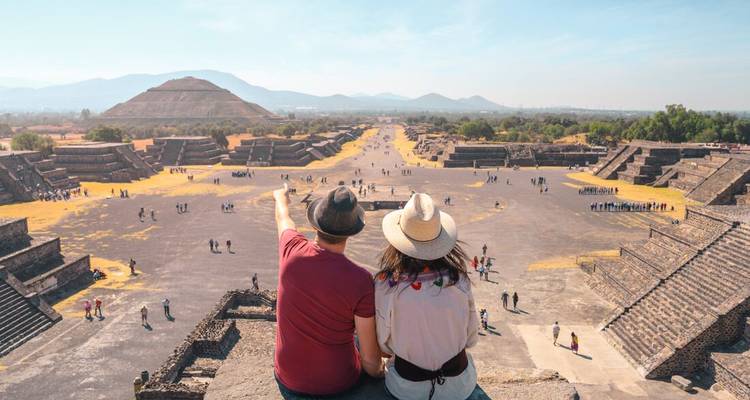 Un couple est assis sur une pyramide antique, regardant les ruines étendues devant eux.