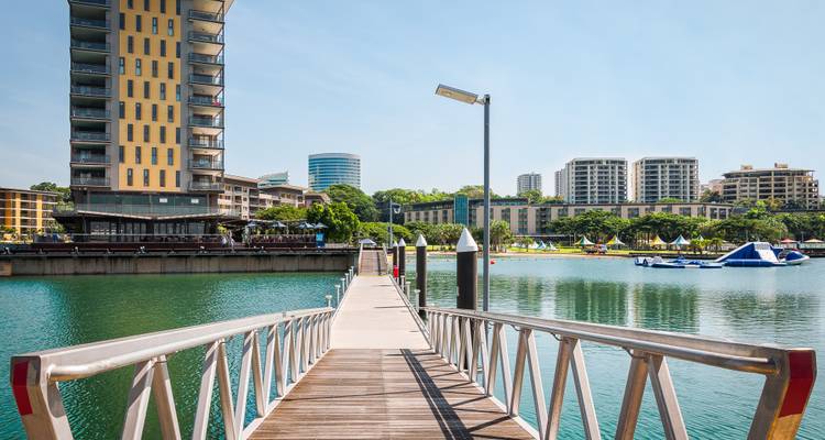 A dock leading to water with modern buildings in the background.