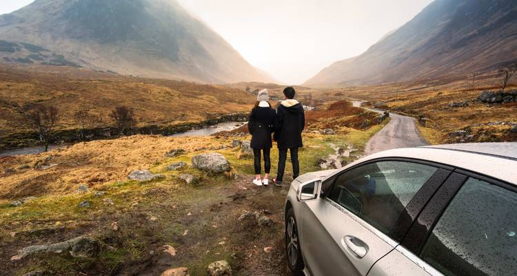 Un couple debout près d'une route avec une vallée pittoresque et des montagnes.