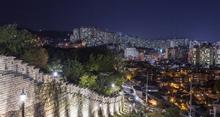 Night view of a city skyline with a historical stone wall.