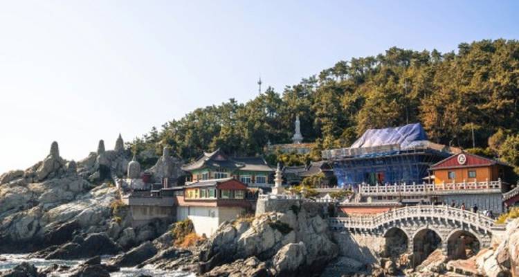 Temple complex on a rocky coast with trees on a hill.