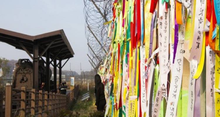 Colorful ribbons tied to a fence with buildings and a person in the background.