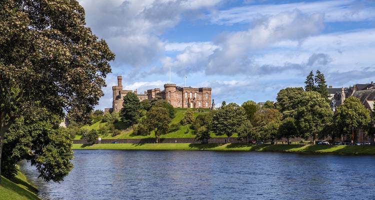 Castle by a river surrounded by trees.