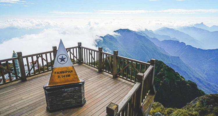 Vue du sommet du Fansipan avec panneau et montagnes nuageuses.
