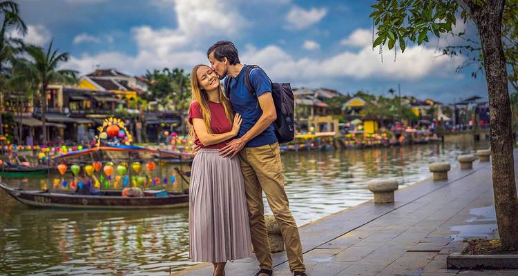 Couple s'embrassant près d'un canal avec des bateaux et des lanternes colorées.