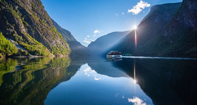 Un bateau naviguant sur un fjord avec des rayons de soleil perçant à travers les montagnes.