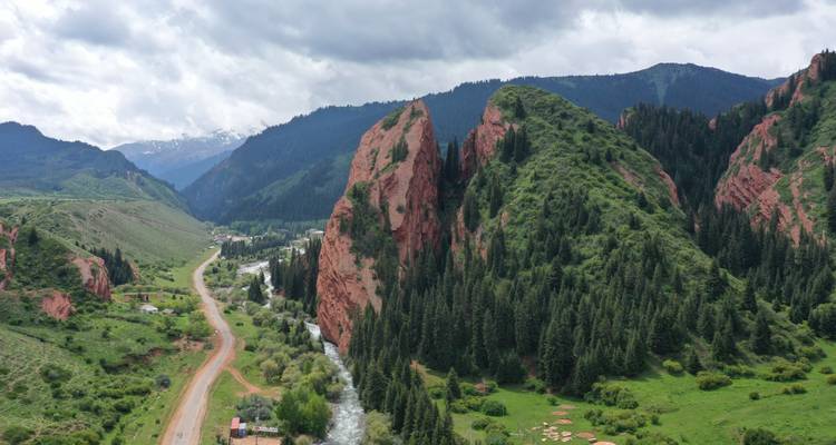 Red rock formations in a lush green valley with trees.