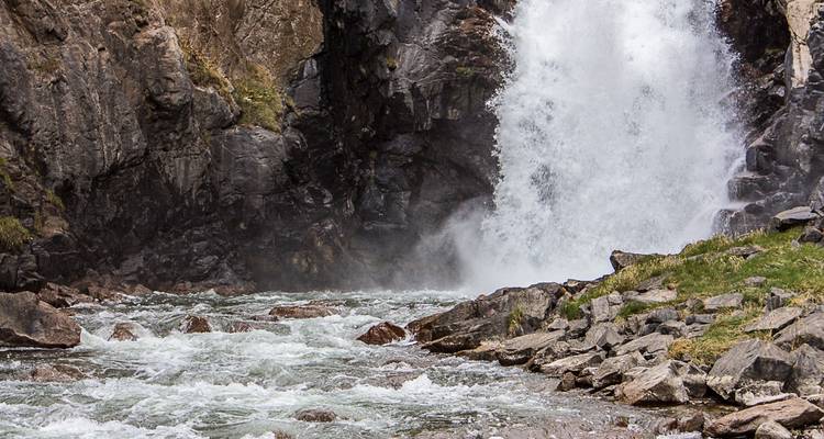 A scenic waterfall cascading into a rocky stream surrounded by rocky cliffs.