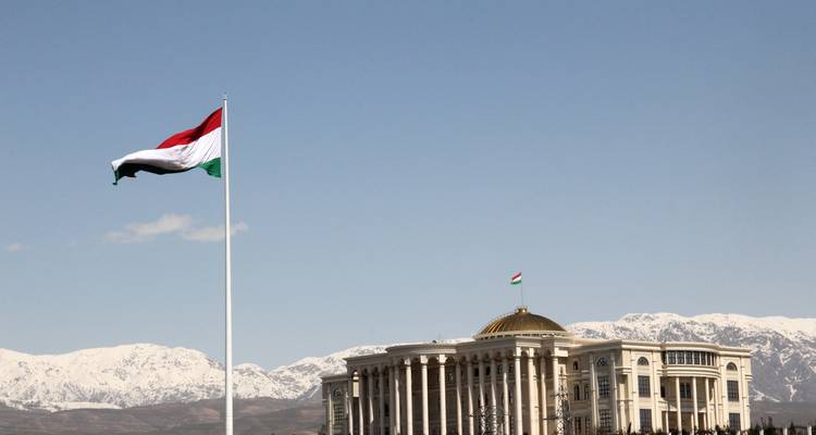 A government building with a flag and snow-capped mountains in the background.