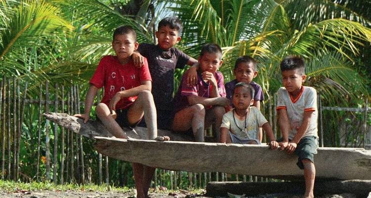 Groupe d'enfants assis sur un bateau en bois avec de la verdure en arrière-plan.