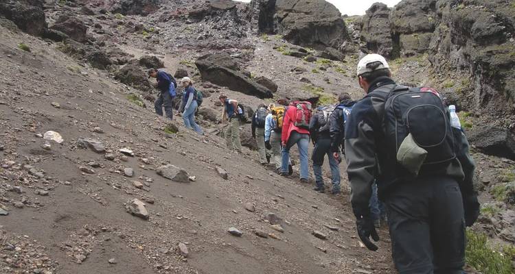 Wandelgroep beklimt een kale vulkanische helling bezaaid met rotsen en as.