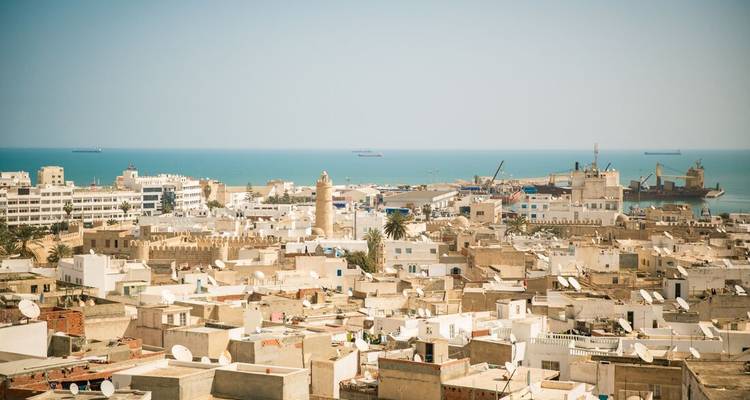 View over a city with white buildings and a clear blue sea.